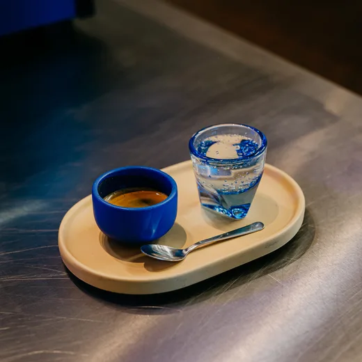 Espresso in a blue cup beside sparkling water on a wooden tray