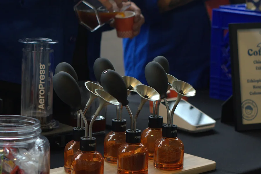 A row of AeroPress brewers and dosing bottles on a competition table