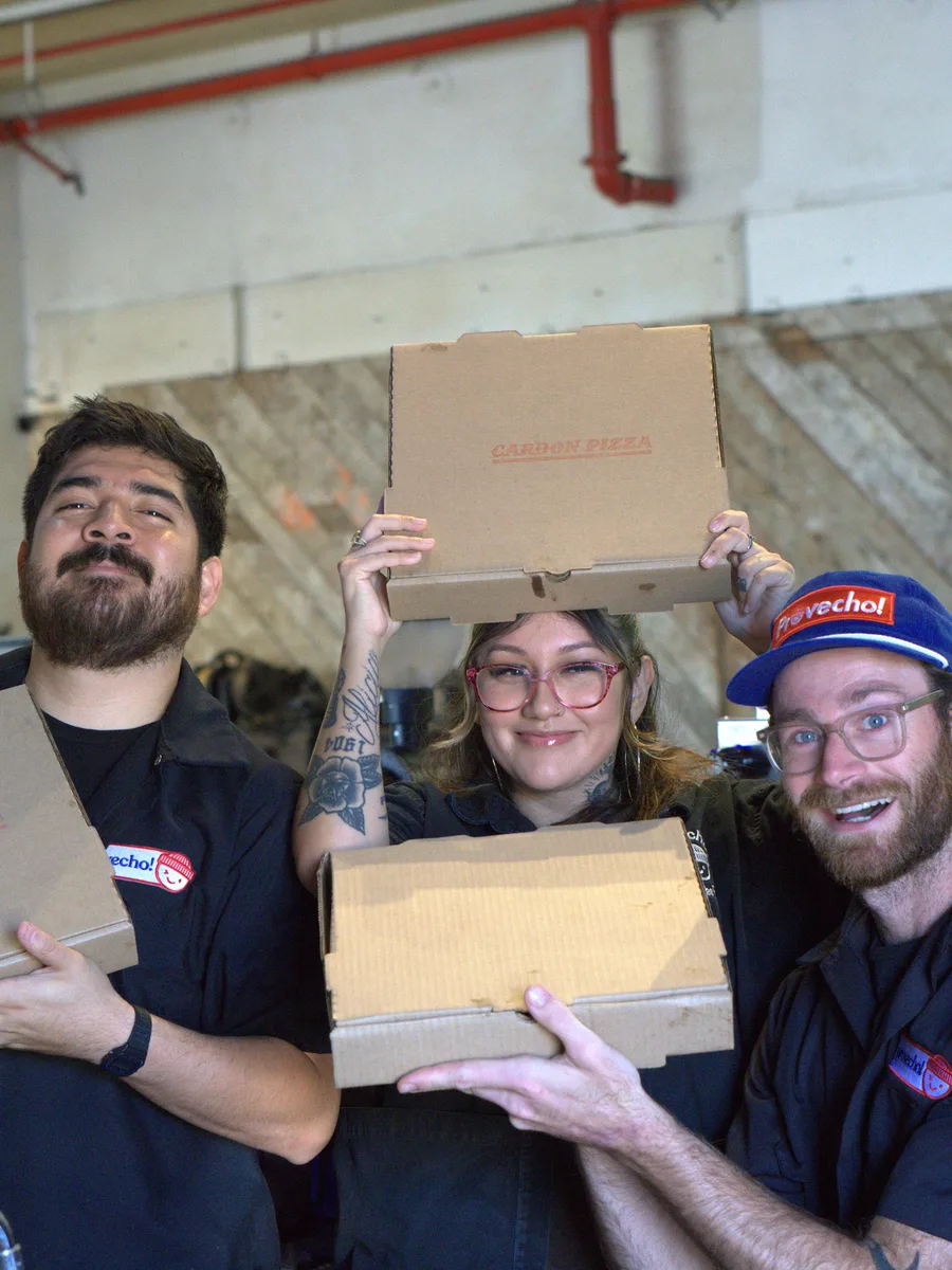 Three people holding up pizza boxes at a pop-up, one in a Provecho cap